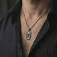 Load image into Gallery viewer, Oxidized Jesus INRI crucifixion pendant necklace worn on the neck, styled in a dark lifestyle portrait with an open shirt and masculine presentation.
