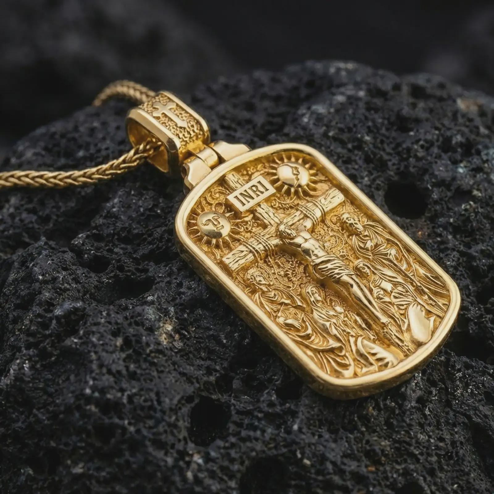 Gold plated Jesus INRI crucifixion pendant necklace presented on porous volcanic rock, highlighting the rectangular devotional form in a luxurious close-up jewelry image.
