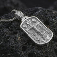 Load image into Gallery viewer, Polished silver Jesus INRI crucifixion pendant necklace displayed on black volcanic rock, shown in a refined macro product shot with detailed crucifix scene and sacred figure relief.

