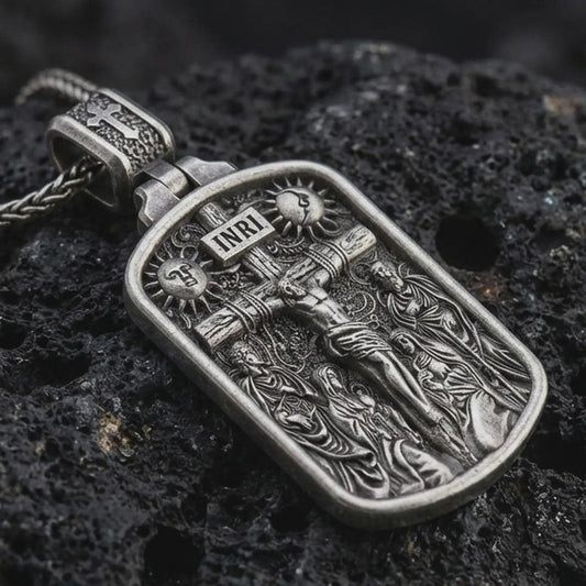 Sterling silver Jesus INRI crucifixion pendant necklace with an oxidized finish resting on textured volcanic rock, captured in a close-up premium studio composition.