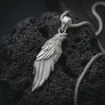 Load image into Gallery viewer, Polished silver raven pendant necklace displayed on black volcanic rock, shown in a refined macro product shot with layered feather detail, open beak, and elongated bird silhouette.

