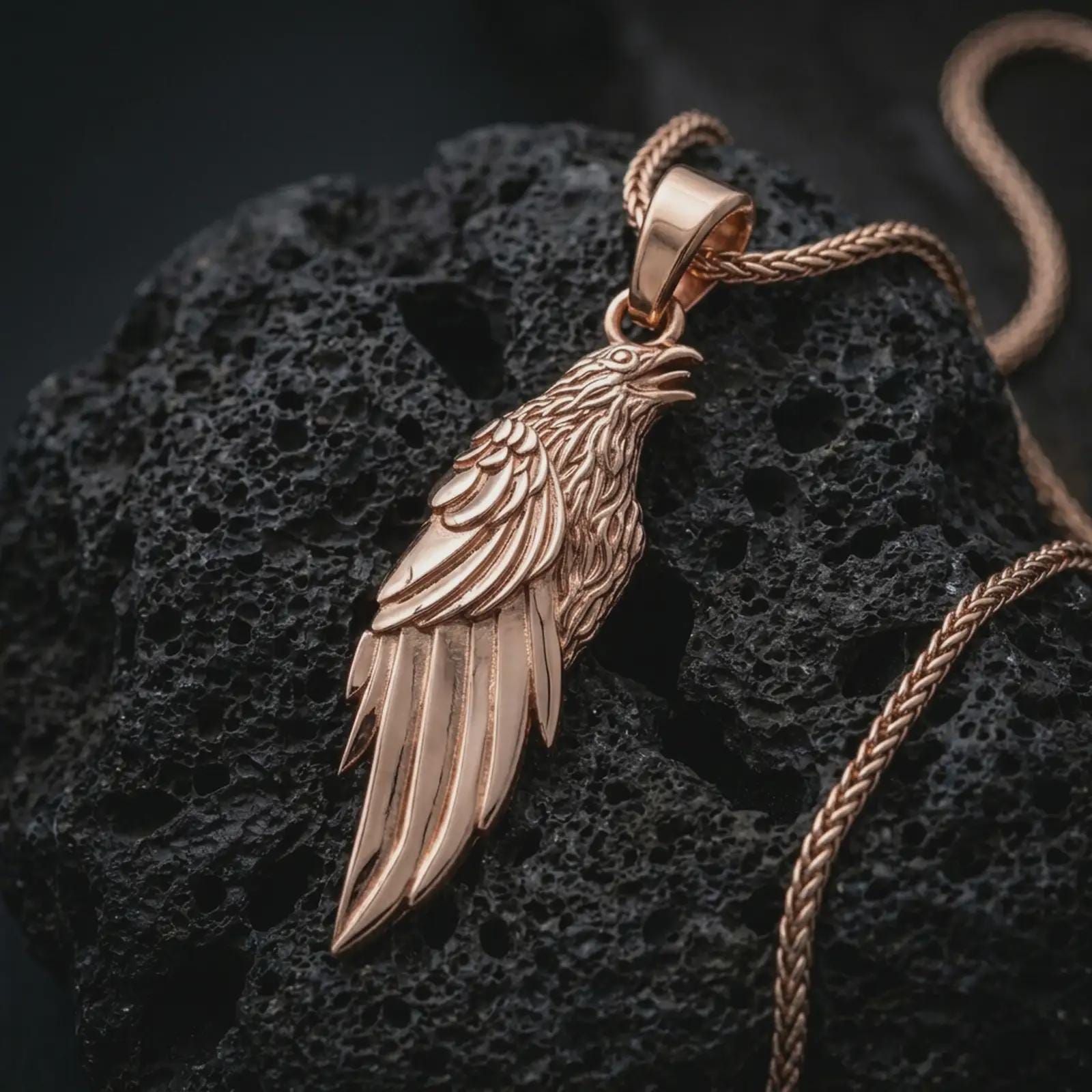 Rose gold plated raven pendant necklace on dark volcanic rock, photographed in a detailed premium studio macro view.