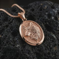 Load image into Gallery viewer, Rose gold plated wolf medallion pendant necklace on dark volcanic rock, photographed in a detailed premium studio macro view.
