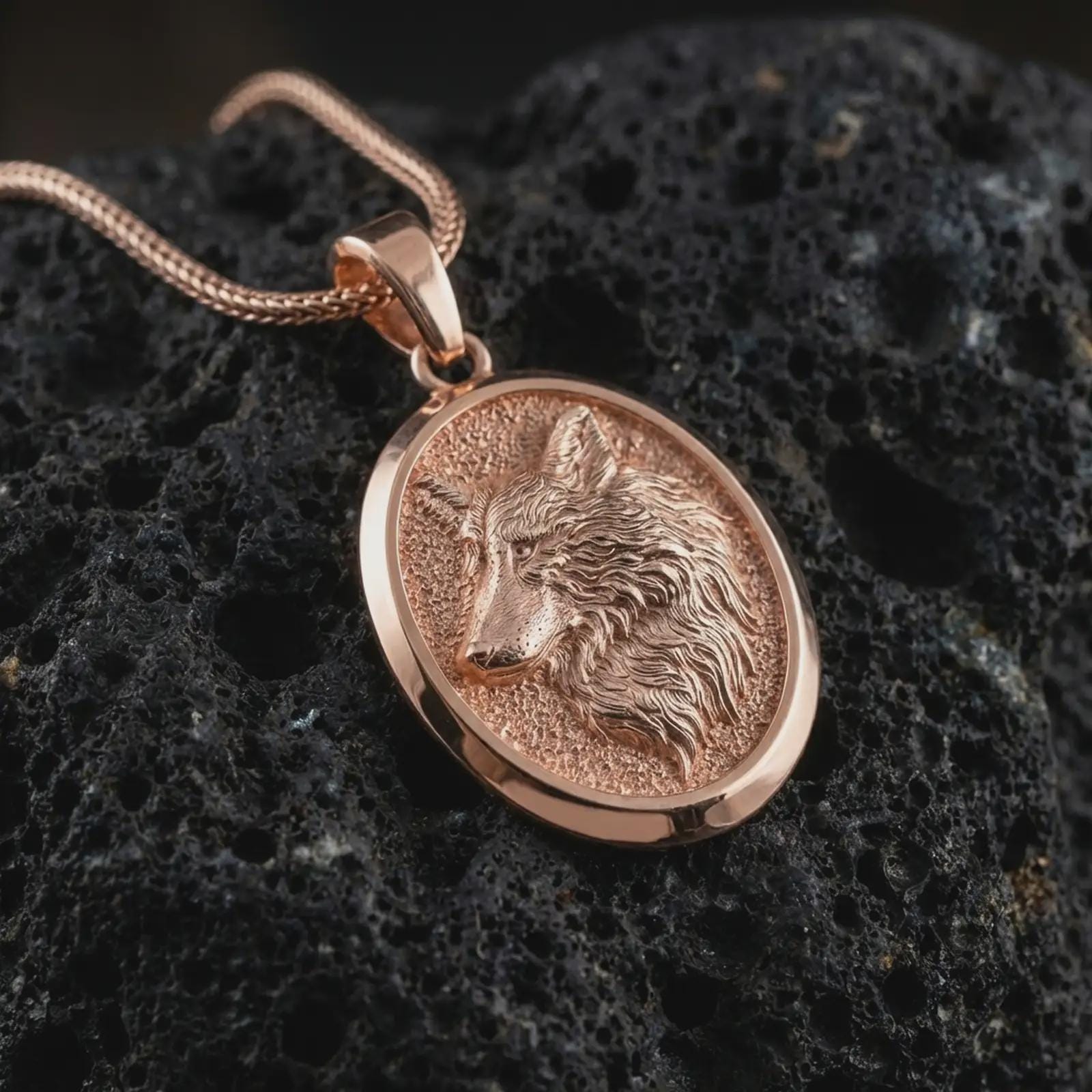 Rose gold plated wolf medallion pendant necklace on dark volcanic rock, photographed in a detailed premium studio macro view.