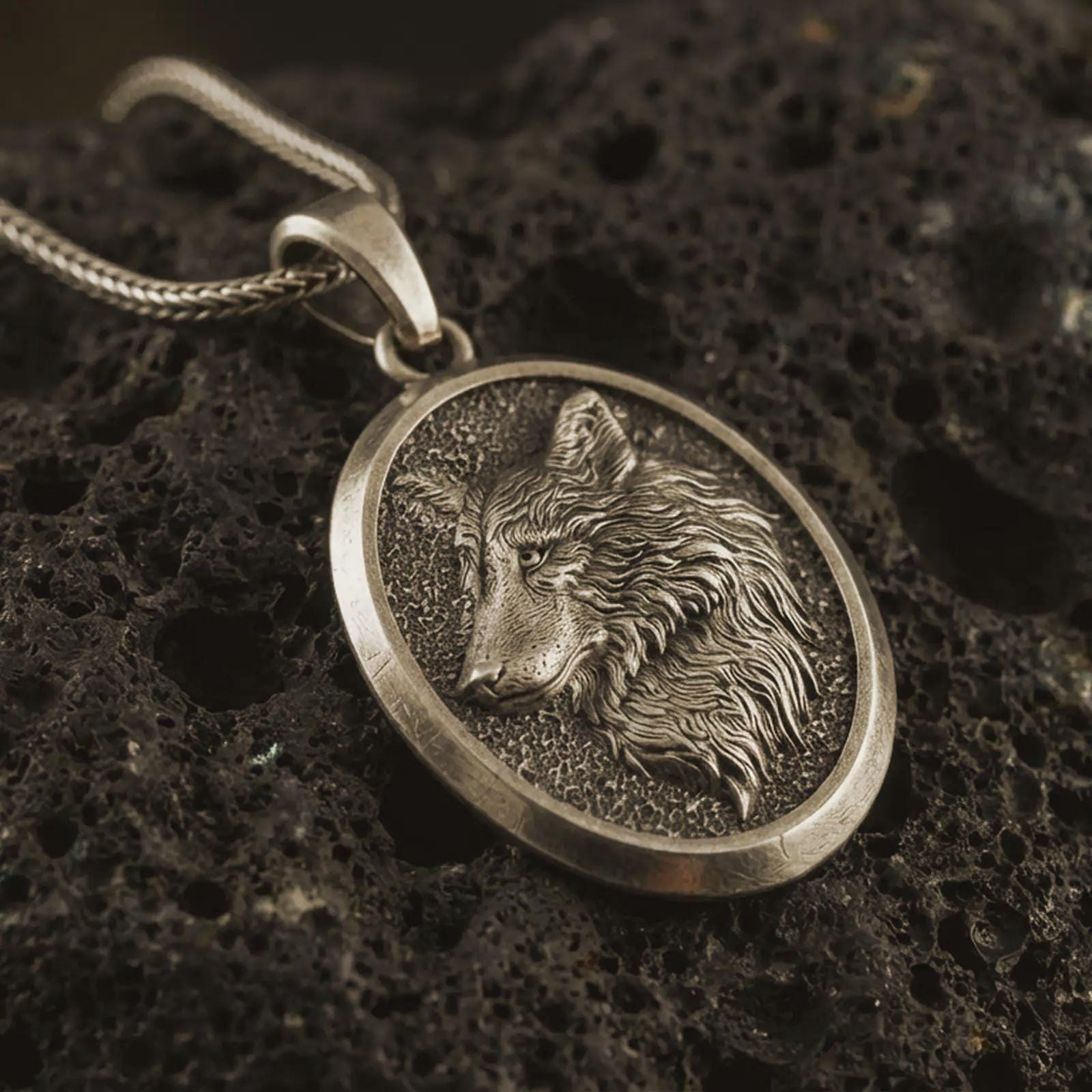 Bronze wolf medallion pendant necklace with an oxidized finish resting on textured volcanic rock, captured in a close-up premium studio composition.