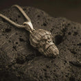 Load image into Gallery viewer, Bronze gorilla head pendant necklace with an oxidized finish resting on textured volcanic rock, captured in a close-up premium studio composition.
