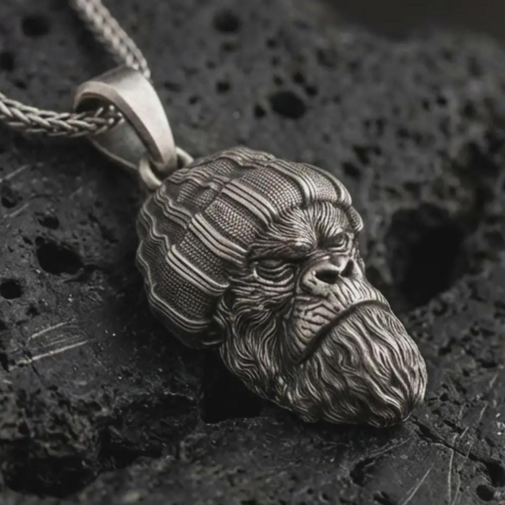 Sterling silver gorilla head pendant necklace with an oxidized finish resting on textured volcanic rock, captured in a close-up premium studio composition.