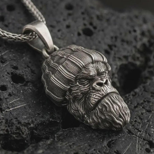 Sterling silver gorilla head pendant necklace with an oxidized finish resting on textured volcanic rock, captured in a close-up premium studio composition.