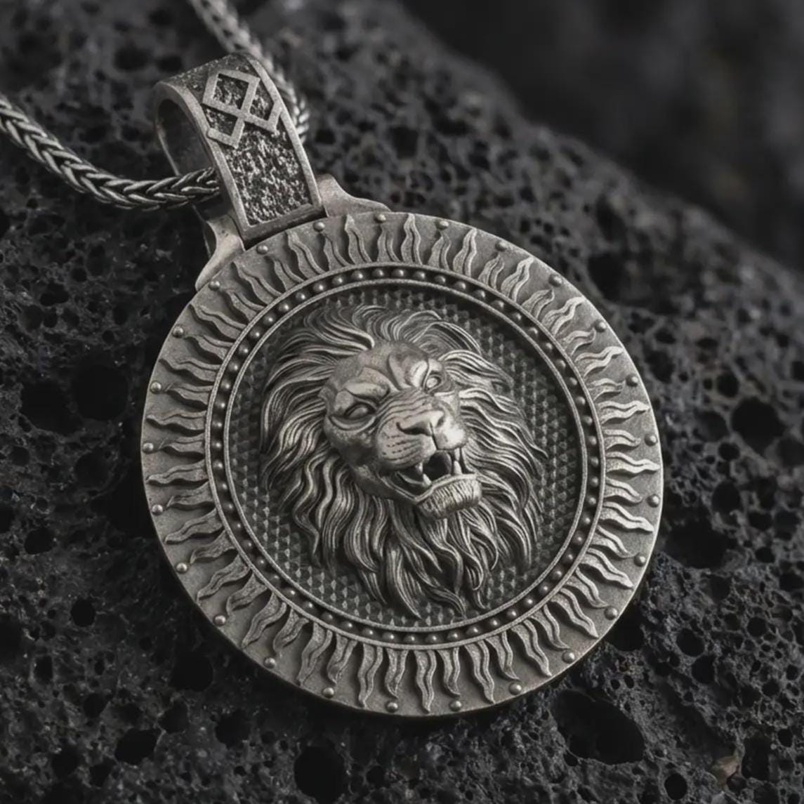Sterling silver Viking lion medallion pendant necklace with an oxidized finish resting on textured volcanic rock, captured in a close-up premium studio composition.