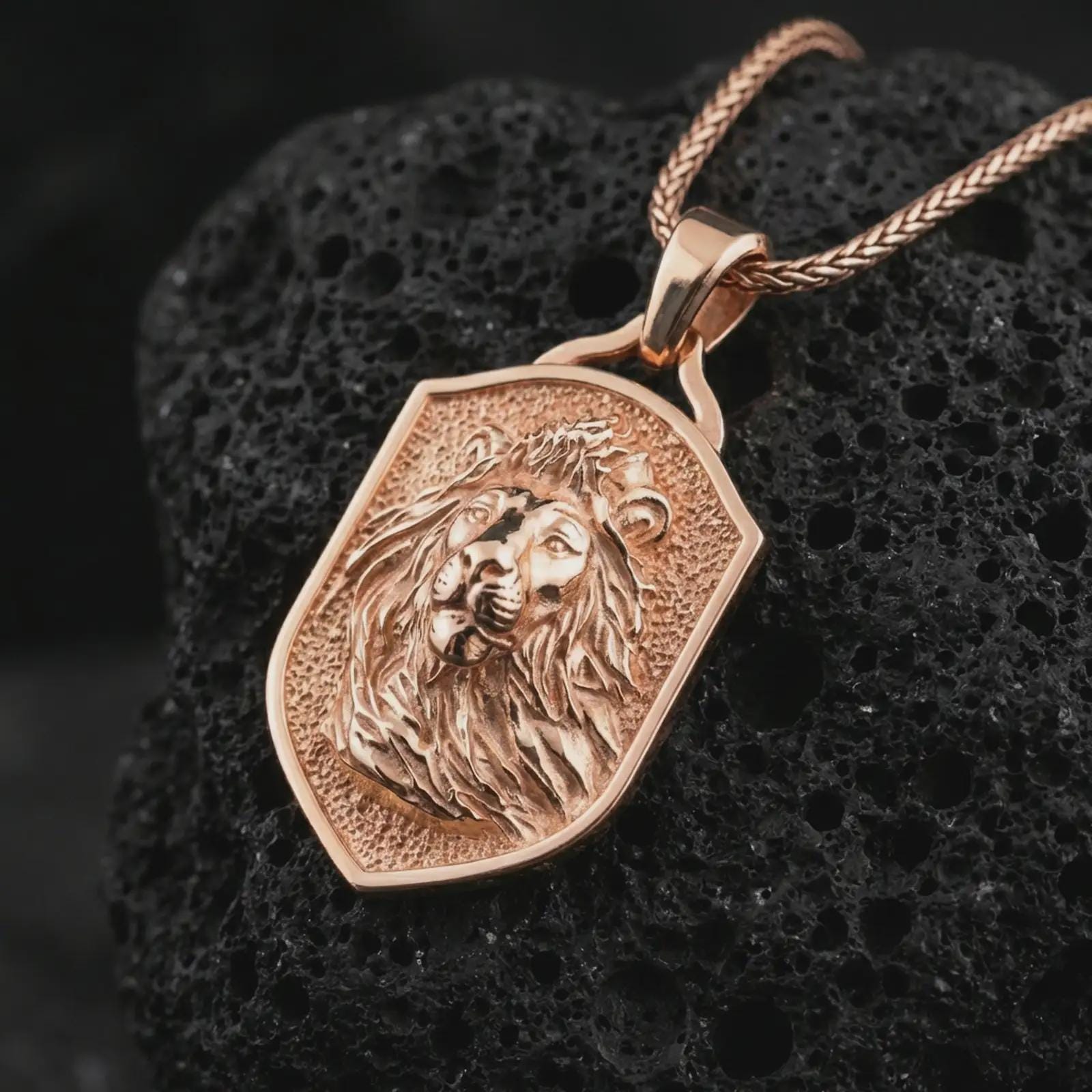 Rose gold plated lion shield pendant necklace on dark volcanic rock, photographed in a detailed premium studio macro view.