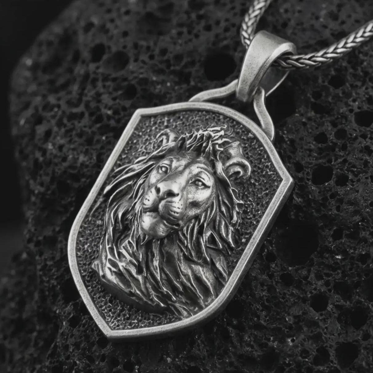 Sterling silver lion shield pendant necklace with an oxidized finish resting on textured volcanic rock, captured in a close-up premium studio composition.