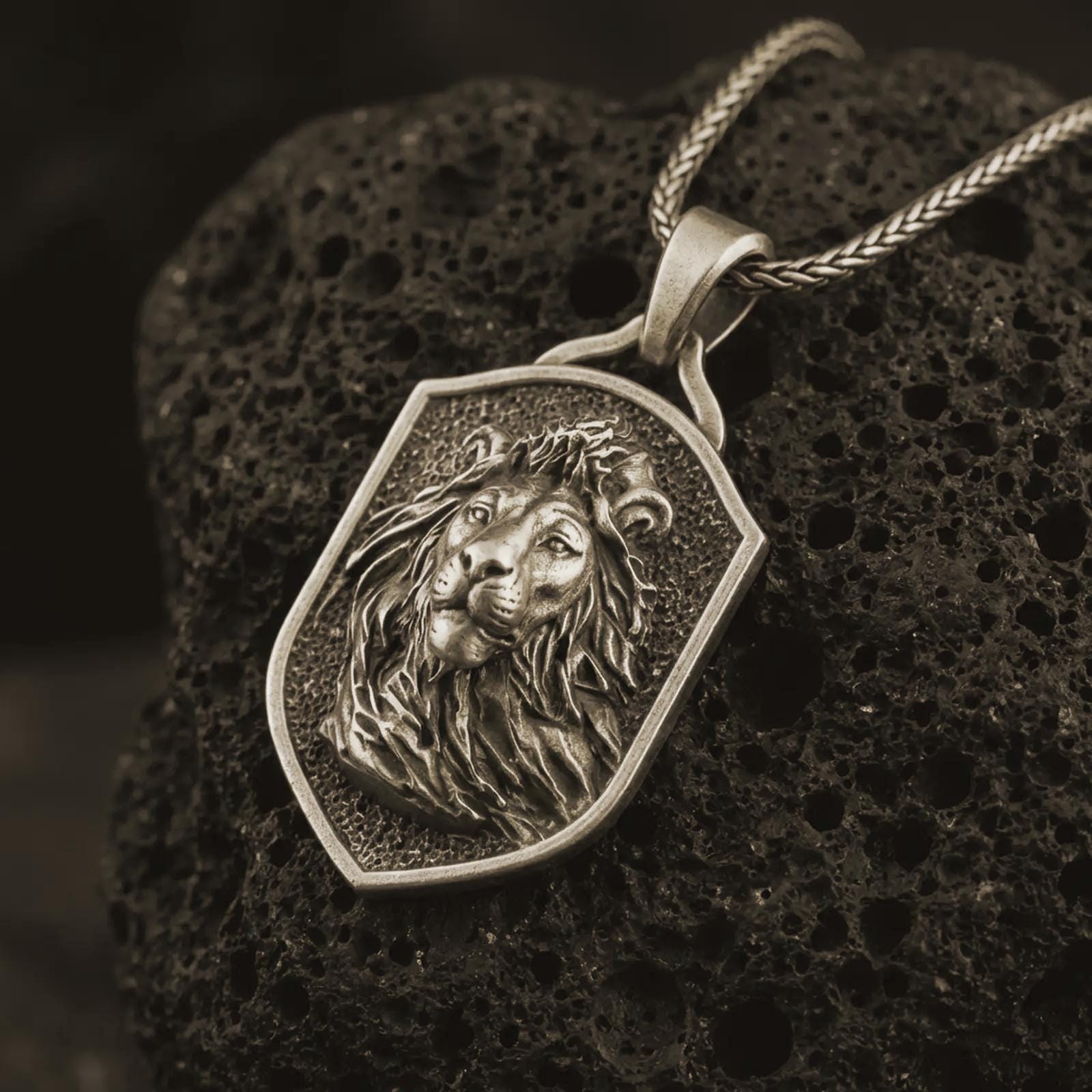 Bronze lion shield pendant necklace with an oxidized finish resting on textured volcanic rock, captured in a close-up premium studio composition.