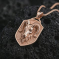 Load image into Gallery viewer, Ram head shield pendant necklace with a rose gold plated finish placed on textured black volcanic rock, shown in a premium close-up image with rich detail and strong zodiac character.
