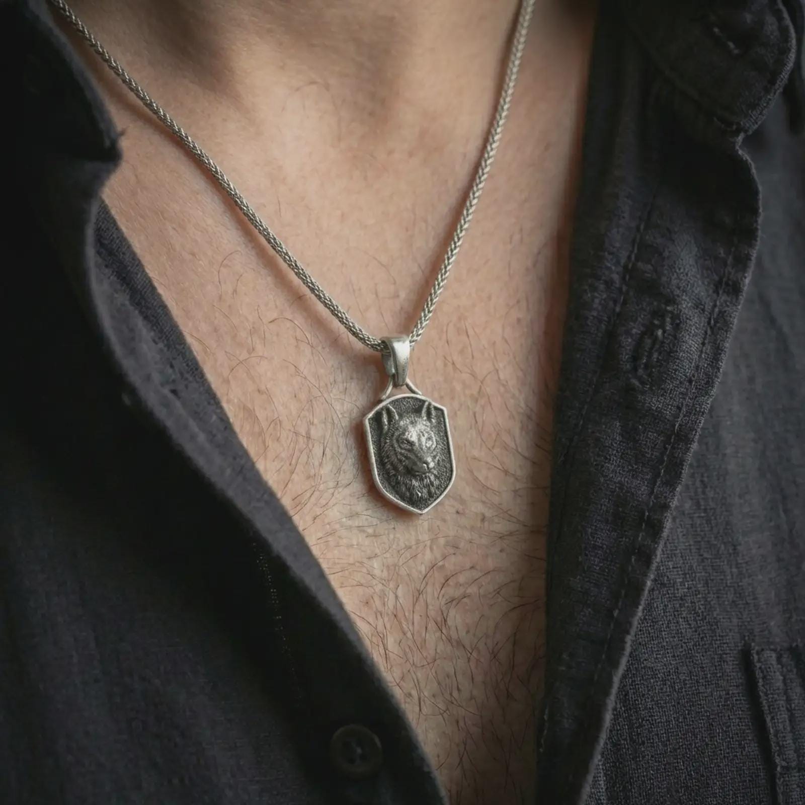 Wolf shield pendant necklace in oxidized sterling silver worn on the neck, styled in a dark lifestyle shot that emphasizes the fierce animal design against the chest.