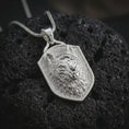 Load image into Gallery viewer, Wolf shield pendant necklace in polished silver displayed on dark volcanic rock, captured in a close-up studio image that highlights the sculpted wolf face and bold protective shield silhouette.
