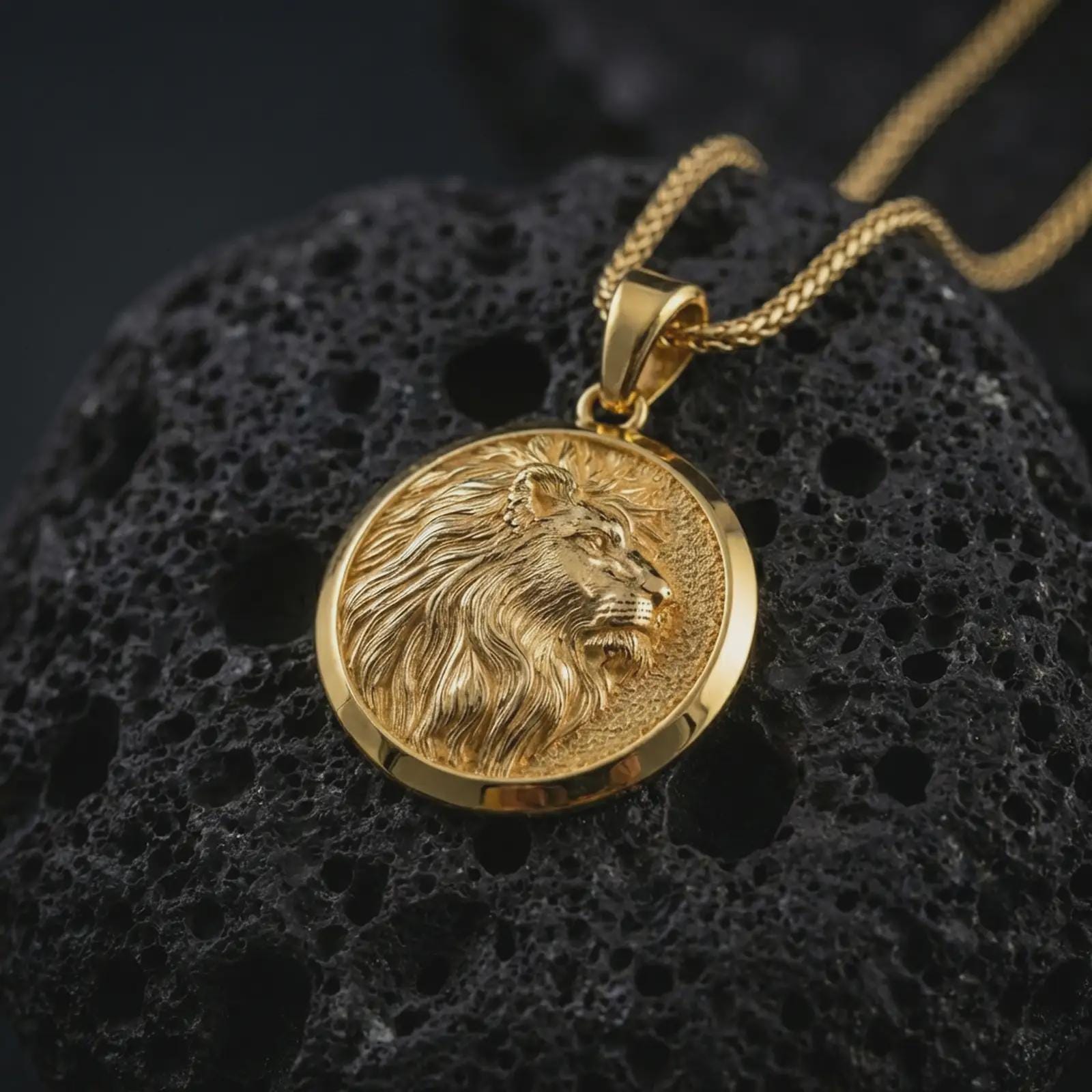 Gold plated lion medallion pendant necklace presented on porous volcanic stone, photographed in a luxurious close-up image that highlights the regal feline motif and detailed mane texture.