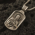 Load image into Gallery viewer, Bronze Saint Peter dog tag pendant necklace with an oxidized finish resting on textured volcanic rock, captured in a close-up premium studio composition.
