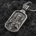Load image into Gallery viewer, Sterling silver Sacred Heart pendant necklace with an oxidized finish resting on textured volcanic rock, captured in a close-up premium studio composition.
