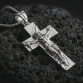Load image into Gallery viewer, Polished silver symbolic cross pendant displayed on black volcanic rock, shown in a refined macro product shot with sculpted female figure and cross relief.
