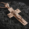 Load image into Gallery viewer, Rose gold plated symbolic cross pendant on dark volcanic rock, photographed in a detailed premium studio macro view.
