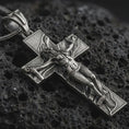 Load image into Gallery viewer, Sterling silver symbolic cross pendant with an oxidized finish resting on textured volcanic rock, captured in a close-up premium studio composition.
