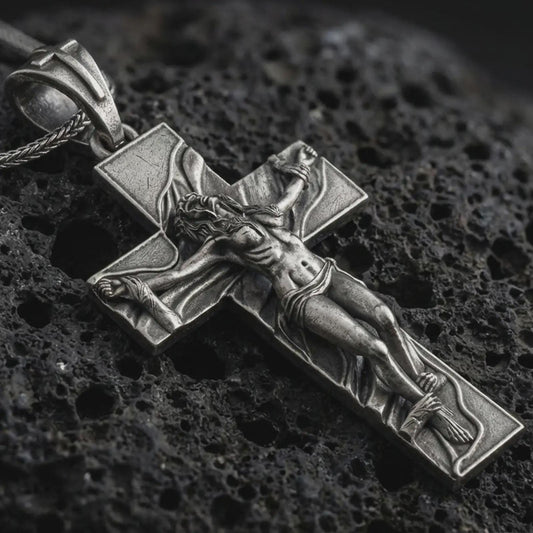 Sterling silver symbolic cross pendant with an oxidized finish resting on textured volcanic rock, captured in a close-up premium studio composition.