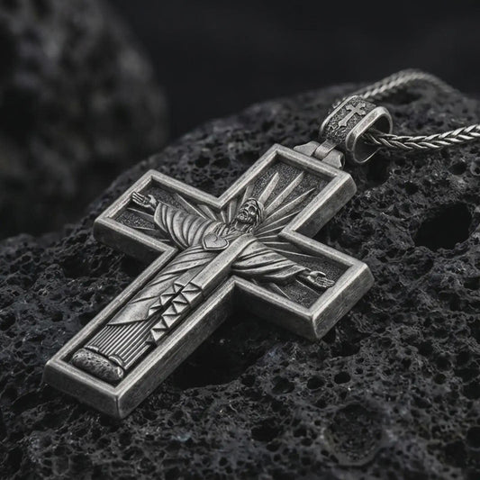 Sterling silver Cristo Protetor cross pendant necklace with an oxidized finish resting on textured volcanic rock, captured in a close-up premium studio composition.