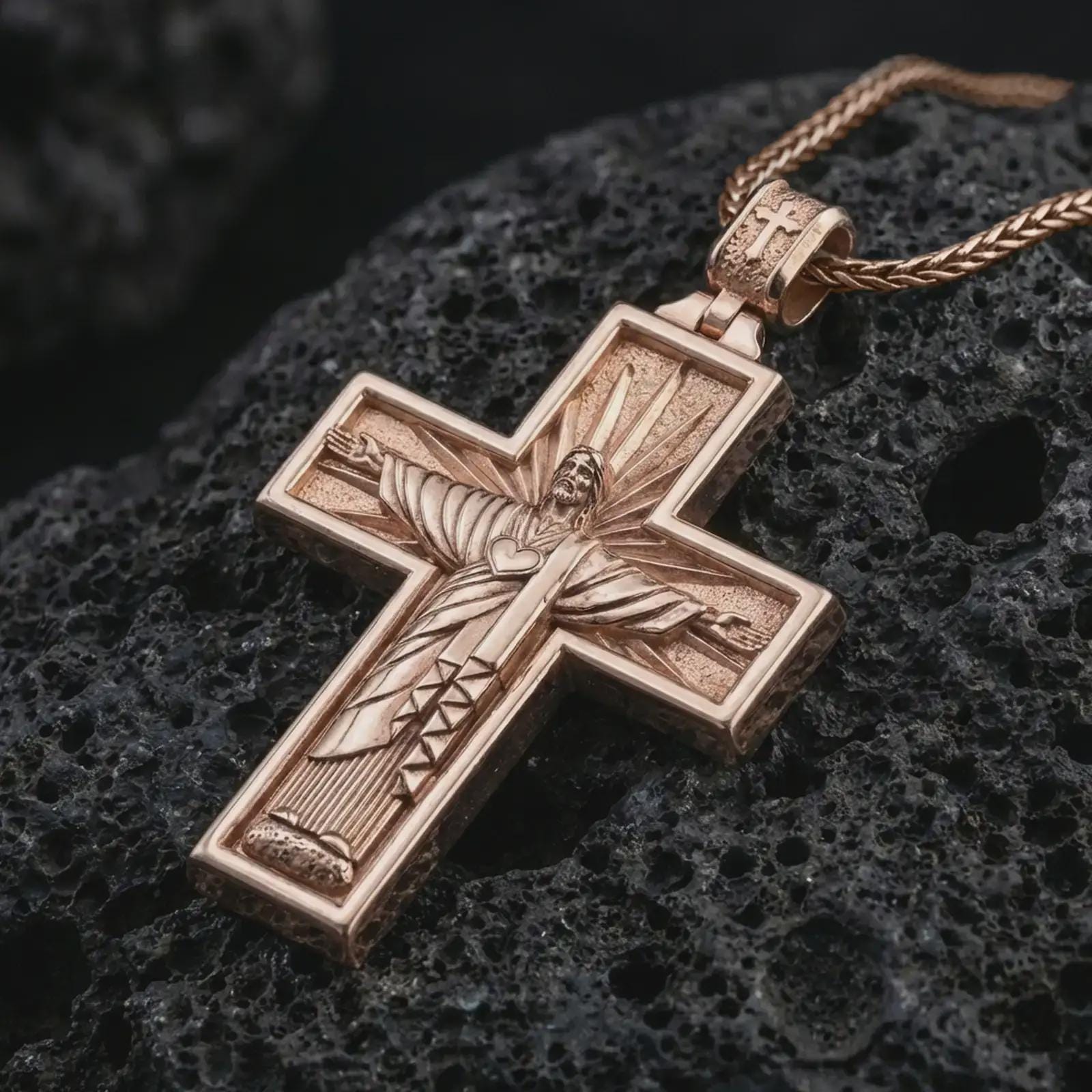 Rose gold plated Cristo Protetor cross pendant necklace on dark volcanic rock, photographed in a detailed premium studio macro view.