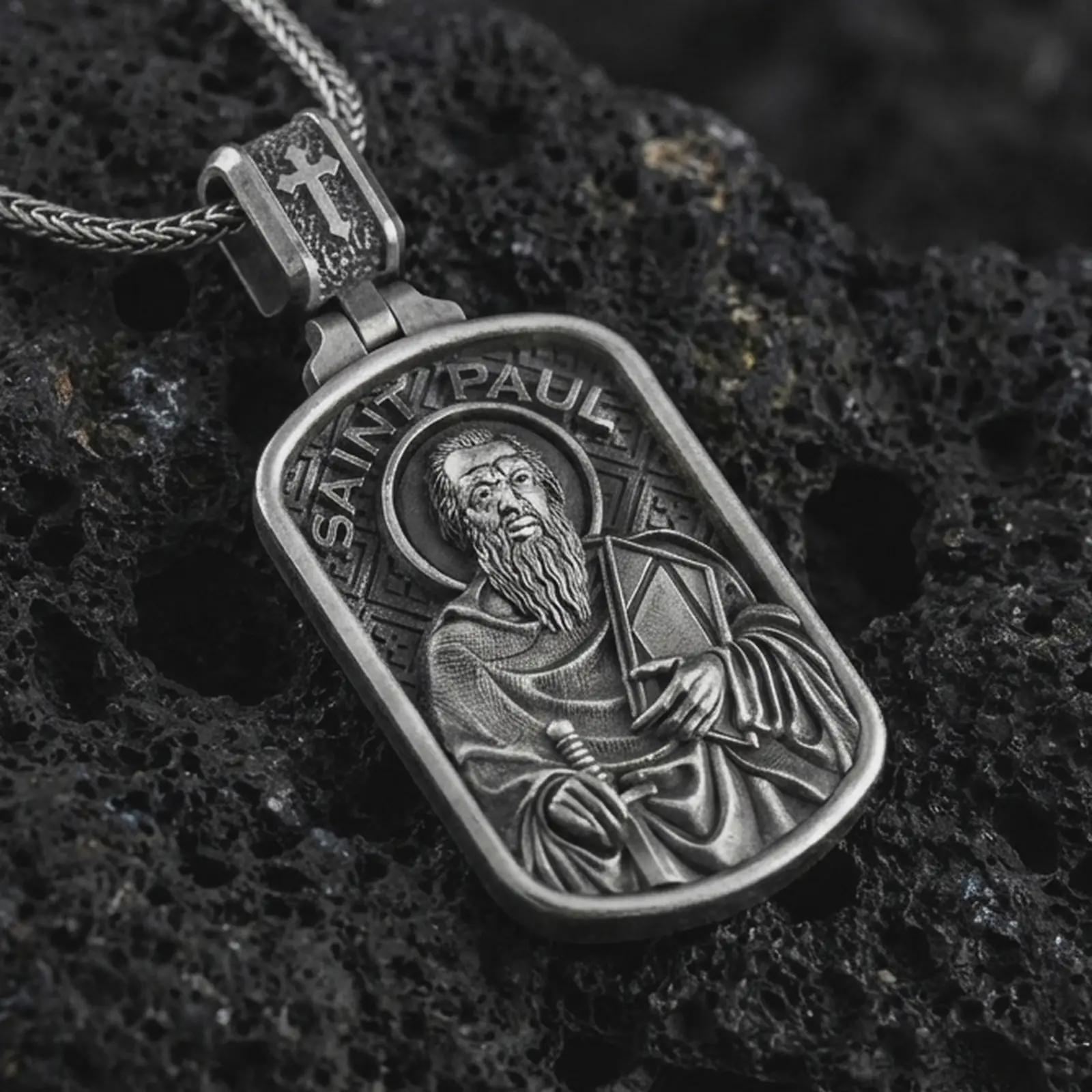 Sterling silver Saint Paul dog tag pendant necklace with an oxidized finish resting on textured volcanic rock, captured in a close-up premium studio composition.