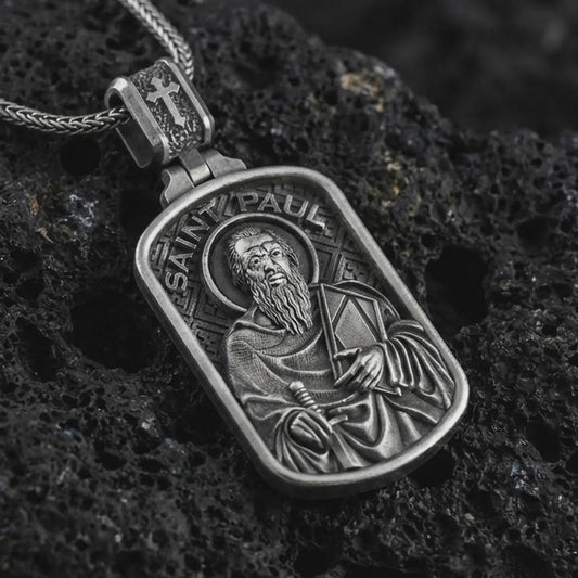 Sterling silver Saint Paul dog tag pendant necklace with an oxidized finish resting on textured volcanic rock, captured in a close-up premium studio composition.