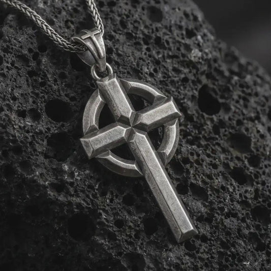 Sterling silver Celtic cross pendant necklace with an oxidized finish displayed on black volcanic stone, captured in a close-up studio image highlighting the bold cross form and circular halo detail.