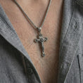 Load image into Gallery viewer, Oxidized crucifix pendant necklace worn on the neck, styled in a dark lifestyle image that highlights the devotional Christian symbol against the chest.
