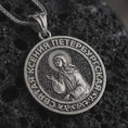 Load image into Gallery viewer, Oxidized Saint Xenia pendant necklace displayed on black volcanic stone, featuring a round Orthodox medal with Saint Ksenia of Petersburg and Cyrillic inscription in a detailed macro product shot.
