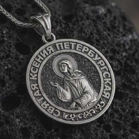 Oxidized Saint Xenia pendant necklace displayed on black volcanic stone, featuring a round Orthodox medal with Saint Ksenia of Petersburg and Cyrillic inscription in a detailed macro product shot.