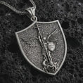 Load image into Gallery viewer, Oxidized Saint Michael pendant necklace displayed on black volcanic stone, featuring a shield-shaped medal with Archangel Michael defeating evil in a detailed macro product photograph.
