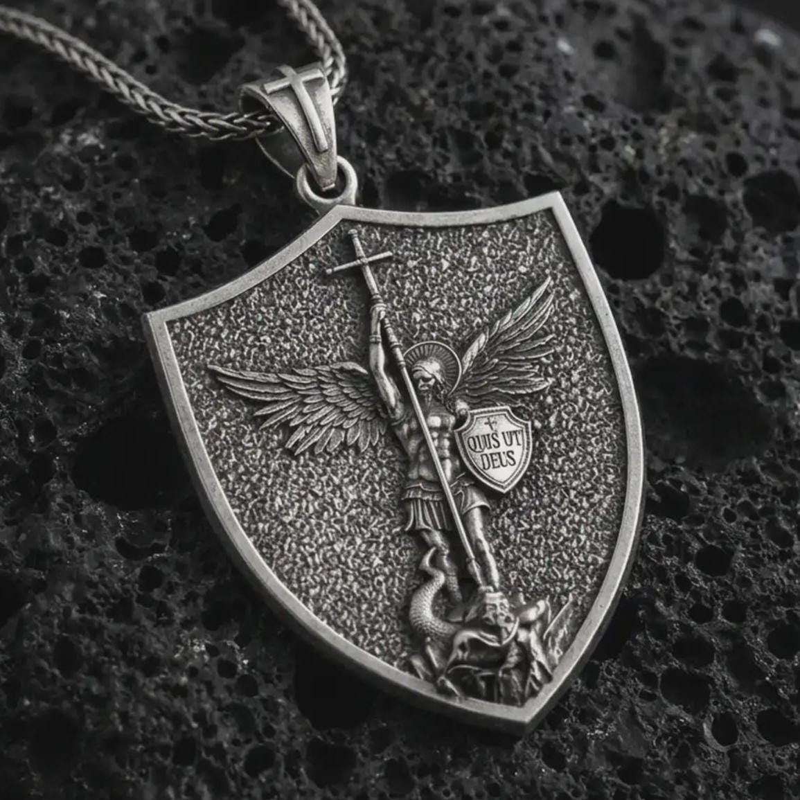 Oxidized Saint Michael pendant necklace displayed on black volcanic stone, featuring a shield-shaped medal with Archangel Michael defeating evil in a detailed macro product photograph.