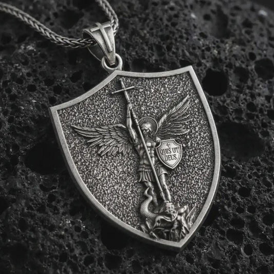 Oxidized Saint Michael pendant necklace displayed on black volcanic stone, featuring a shield-shaped medal with Archangel Michael defeating evil in a detailed macro product photograph.