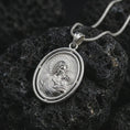 Load image into Gallery viewer, Polished silver Madonna and Child pendant necklace displayed on dark volcanic rock, highlighting the sacred mother and infant motif within an elegant oval religious medal design.
