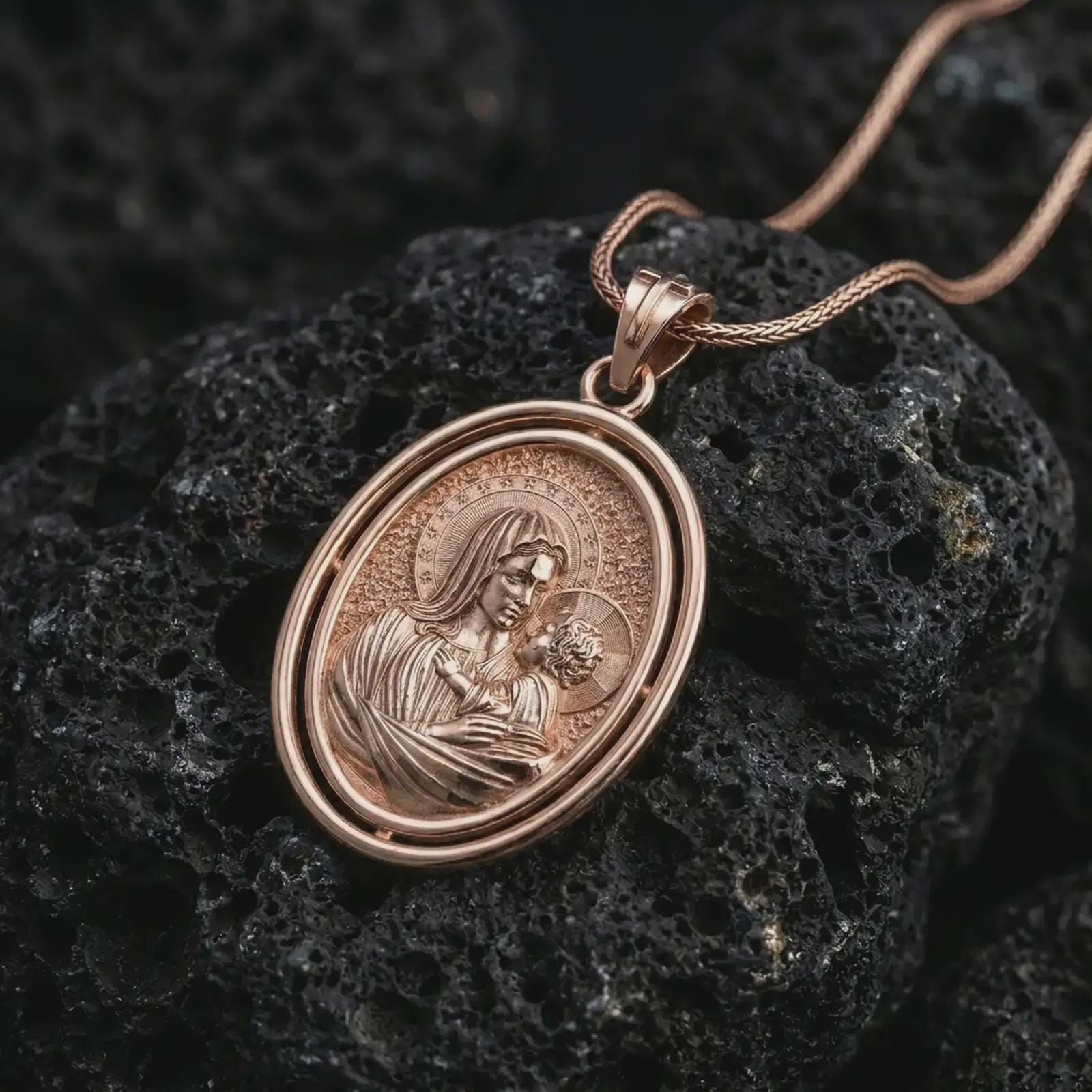 Rose gold plated Madonna and Child pendant necklace presented on porous volcanic stone, showcasing the layered oval frame and tender holy mother and child relief in a luxury macro image.