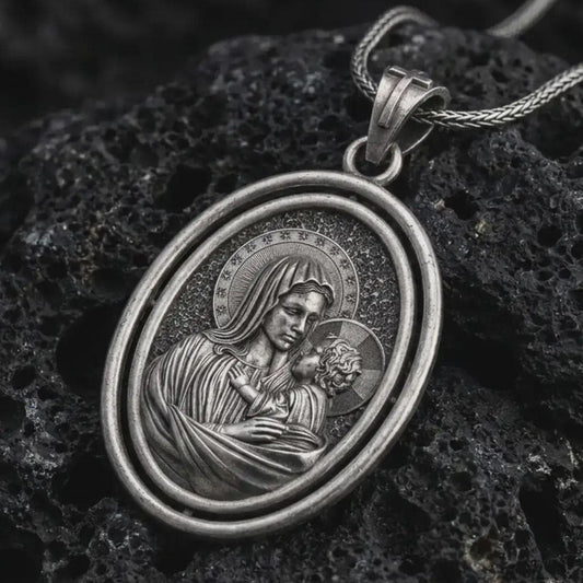 Oxidized Madonna and Child pendant necklace resting on black volcanic stone, featuring an oval double-frame medallion with the Virgin Mary holding baby Jesus in a detailed devotional relief.