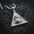 Load image into Gallery viewer, Polished silver all-seeing eye pendant necklace displayed on black volcanic rock, shown in a refined macro product shot with realistic eye relief and triangular frame detail.
