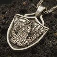 Load image into Gallery viewer, Bronze Fortiores Una eagle shield pendant necklace with an oxidized finish resting on textured volcanic rock, captured in a close-up premium studio composition.
