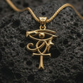 Load image into Gallery viewer, Gold plated Eye of Ra and Ankh pendant necklace presented on porous volcanic rock, highlighting the sacred protective motif in a luxurious close-up jewelry image.

