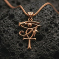 Load image into Gallery viewer, Rose gold plated Eye of Ra and Ankh pendant necklace on dark volcanic rock, photographed in a detailed premium studio macro view.
