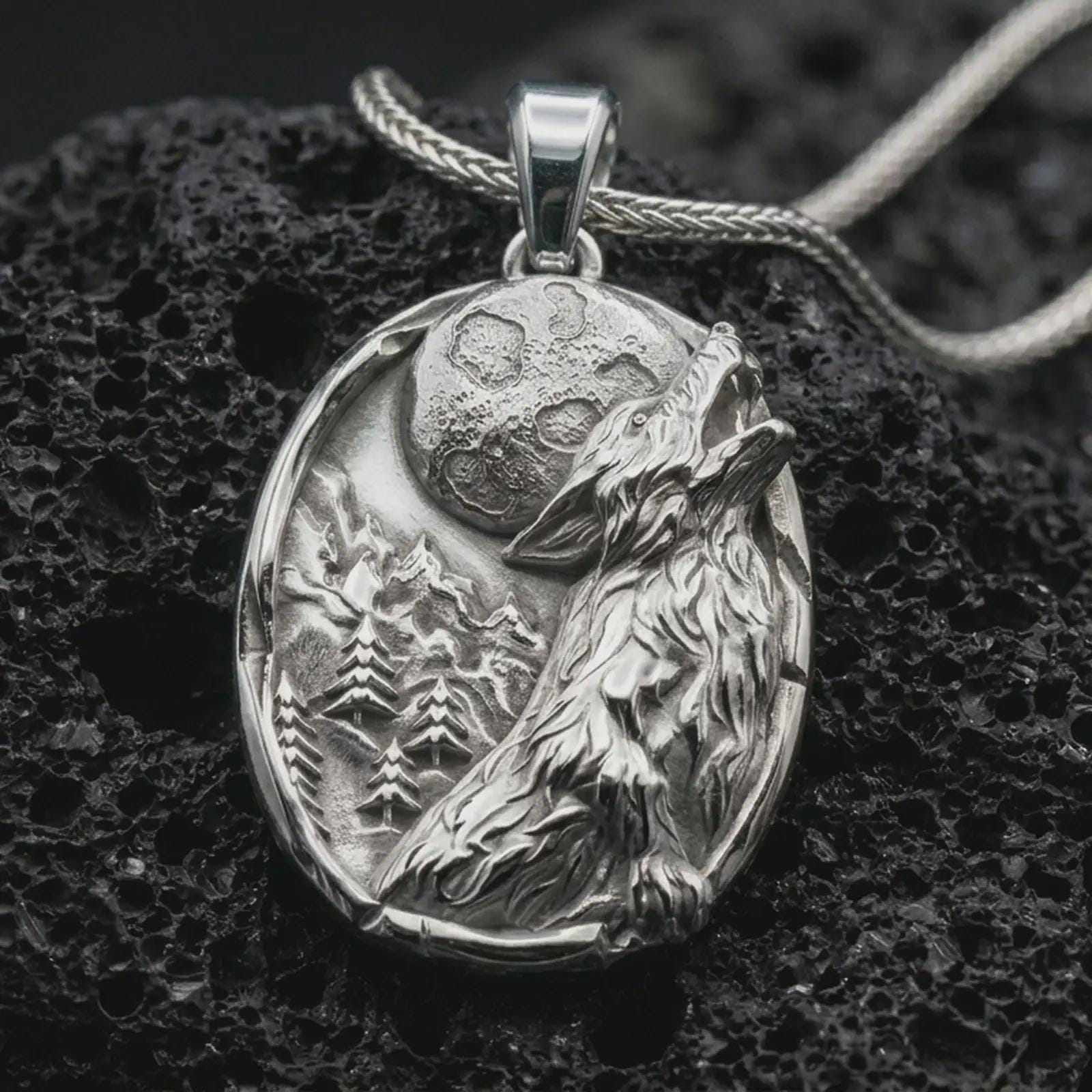 Polished silver howling wolf pendant necklace displayed on black volcanic rock, shown in a refined macro product shot with detailed lunar, mountain, and fur relief.