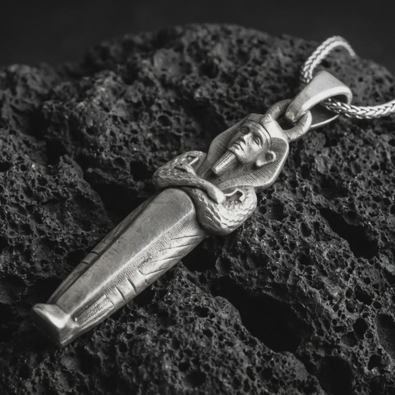Sterling silver King Tut pendant necklace with an oxidized finish resting on textured volcanic rock, captured in a close-up premium studio composition.