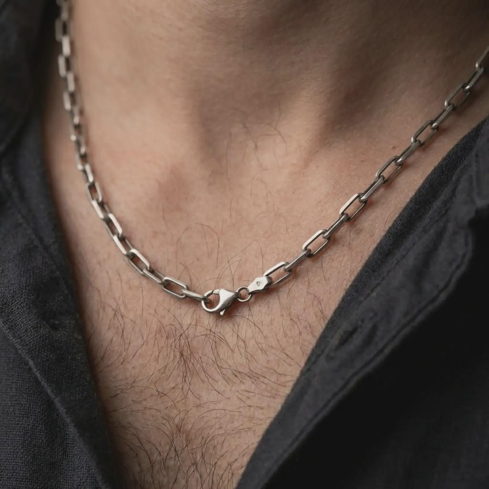 Oxidized cable link chain necklace worn on the neck, styled in a dark lifestyle portrait with an open shirt and masculine presentation.