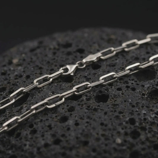 Sterling silver cable link chain necklace with an oxidized finish resting on textured volcanic rock, captured in a close-up premium studio composition.