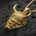 Load image into Gallery viewer, Gold plated Oni mask pendant necklace presented on porous volcanic rock, highlighting the fierce demonic face and ornamental surface detail in a luxurious close-up jewelry image.
