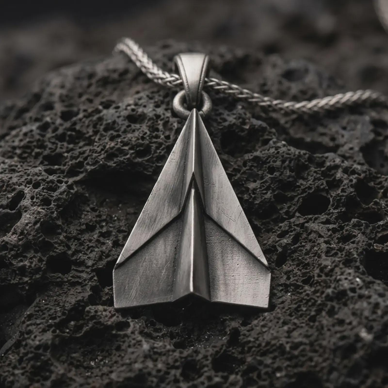 Sterling silver origami airplane pendant necklace with an oxidized finish resting on textured volcanic rock, captured in a close-up premium studio composition.
